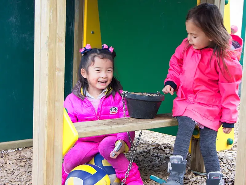 Two girls laughing together on a playground swing seat